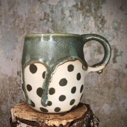 Hohe bauchige handgetöpferte Tasse aus hellem Ton mit grünen Punkten. Im oberen Bereich mit einer üppigen, grünen Glasur, die in dicken Tropfen herabläuft.